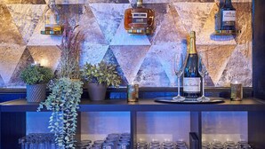A bar area with a geometric patterned wall, bottles of liquor, glasses, and potted plants. - Bungalow in France with Private Garden (Mauroux)
