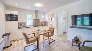 A modern kitchen with a built-in oven, a stone backsplash, and a dining area with a table and chairs. - Bungalow in France with Private Garden (Mauroux)