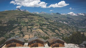 Un refugio de montaña con cabañas de madera, vista de las colinas y montañas circundantes, y un cielo despejado.