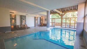 Una piscina interior con paredes de piedra, sillones de descanso y ventanas amplias.