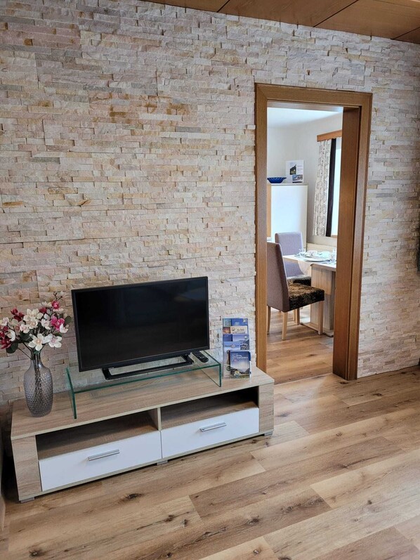 A modern living room with a stone wall, a glass TV stand, a flat-screen TV, a vase with flowers, and a wooden door leading to another room. - Pure relaxation - whether in summer or winter in Mayrhofen in the Zillertal (Schwendau)