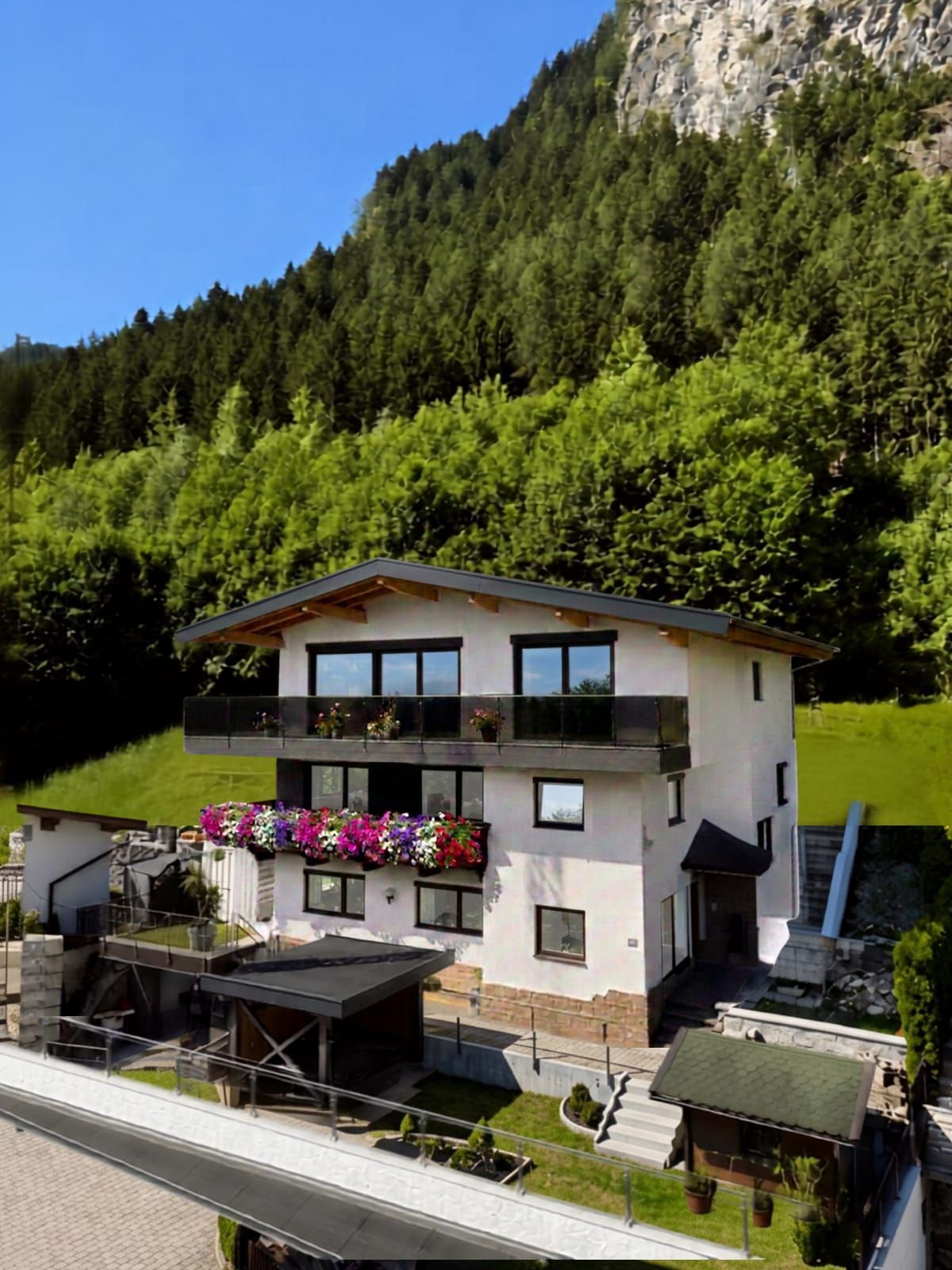 Um edifício moderno de dois andares com varandas, rodeado por vegetação exuberante e um cenário montanhoso.