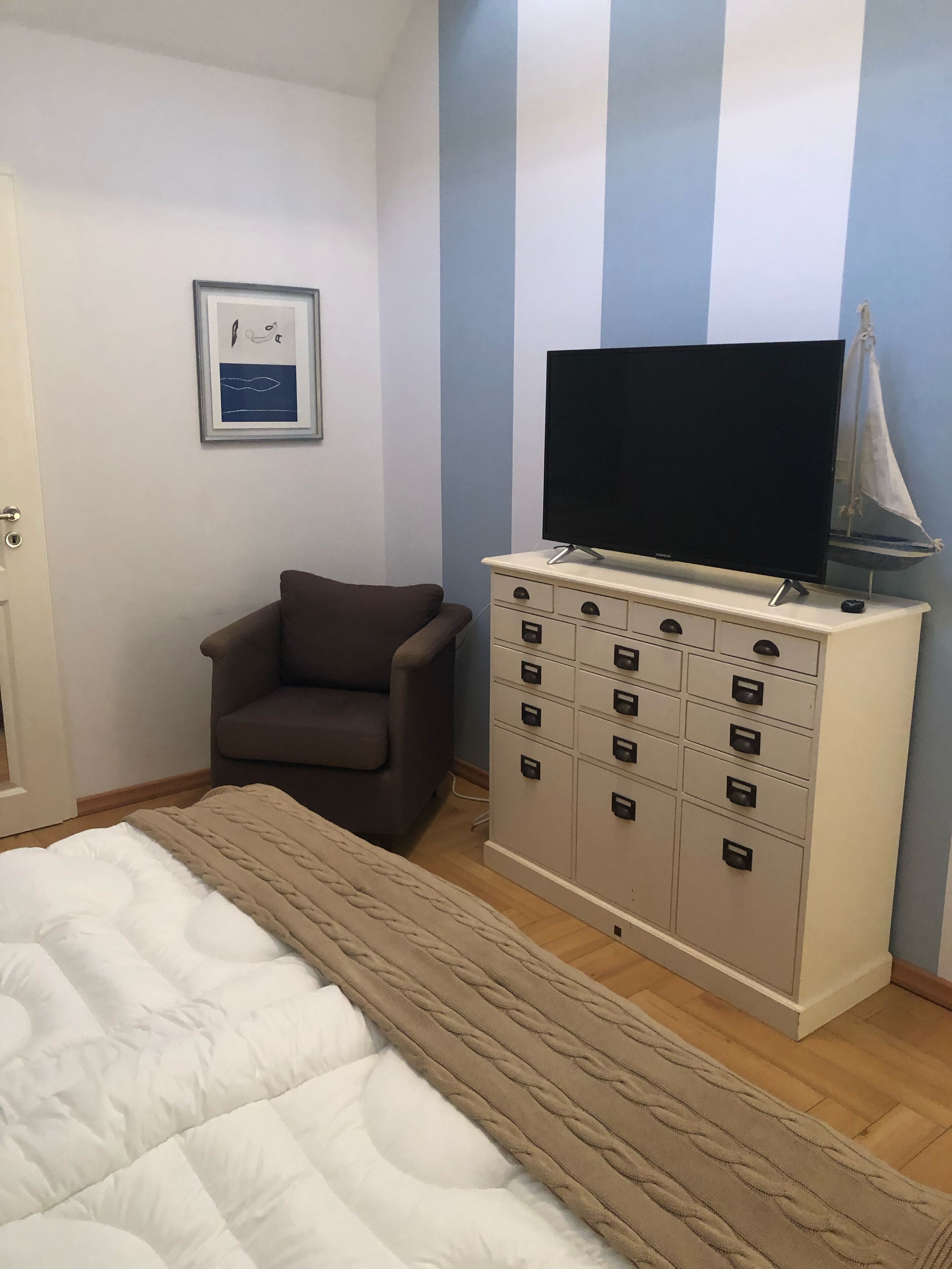 A bedroom with a bed, a chair, a TV on a cabinet, and a framed picture on the wall.