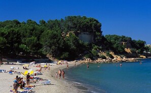 Una platja amb gent que pren el sol i nedant, envoltada d'arbres i penya-segats.