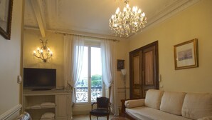 A living room with a sofa, a television, a chandelier, and a window with curtains. - Luxury apartment at the heart of Paris Rent (Paris)