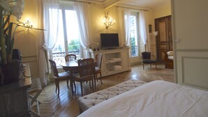 A hotel room with a bed, a dining table with chairs, a TV on a cabinet, and a balcony with curtains. - Luxury apartment at the heart of Paris Rent (Paris)