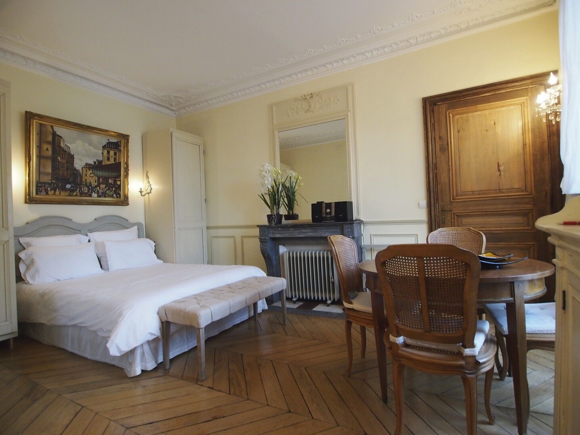 Ein Hotelzimmer mit Bett, kleinem Tisch mit Stühlen, Heizkörper, Spiegel und Holztür.