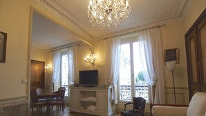 A spacious living room with a chandelier, a television, and a balcony with a wrought iron railing. - Luxury apartment at the heart of Paris Rent (Paris)
