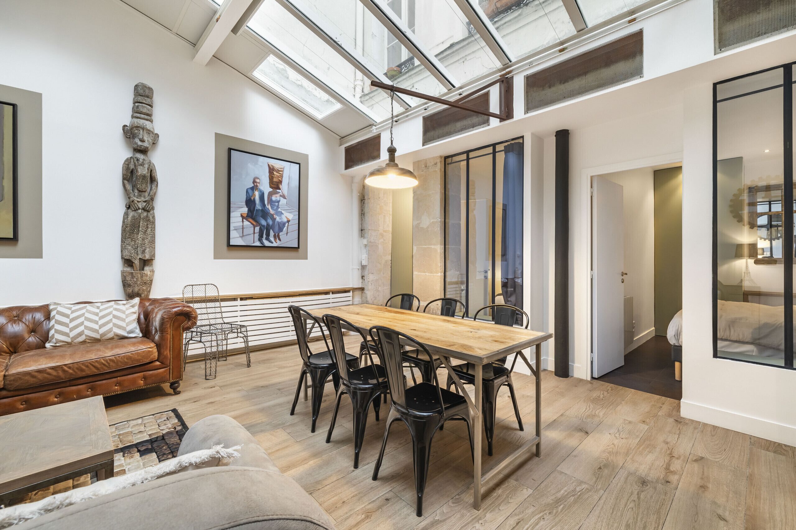 A spacious living area with a wooden dining table, leather sofa, and a large window.