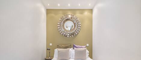 Een slaapkamer met een groot bed, een ronde spiegel en een nachtkastje met een lamp.