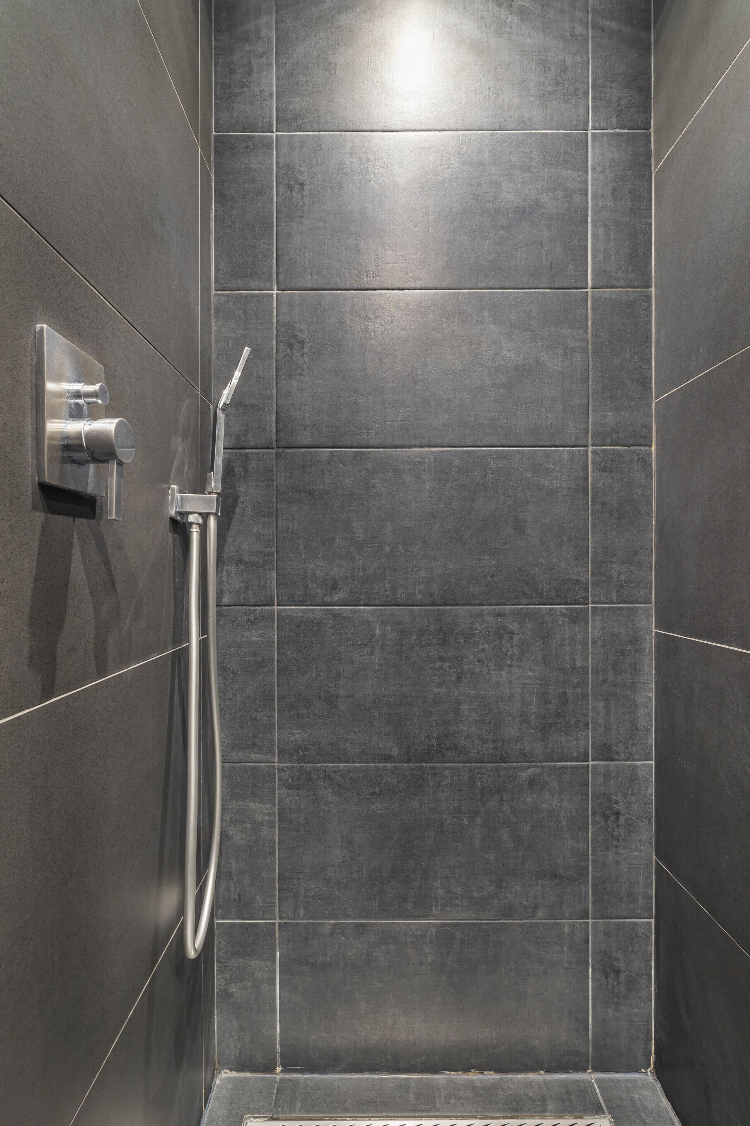 A shower area with dark tiles and a modern showerhead.
