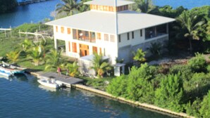 A two-story house with a flat roof, located near a body of water with boats docked. - Beautiful Beachfront Island Home, Private Dock, Village Transportation Included (Placencia)