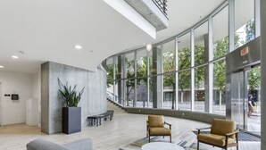 A modern lobby with a curved glass wall, seating area, and a staircase leading to an upper level. - Pearl Pad: Enjoy River, Shopping, Dining.  Balcony, Garage  and free EV chging! (Portland)