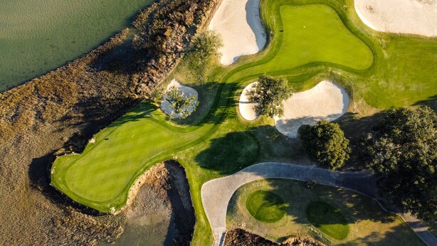An aerial view of a golf course with sand bunkers, water hazards, and a well-maintained green.