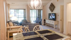 A living room with a sofa, patterned chairs, a glass coffee table, a television, and a chandelier.