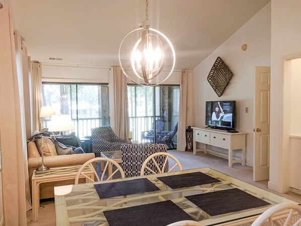 A living room with a sofa, patterned chairs, a glass coffee table, a television, and a chandelier.