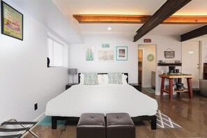 Une chambre à coucher avec un grand lit, un plafond en bois, une petite kitchenette et une salle de bain visible à travers une porte ouverte.