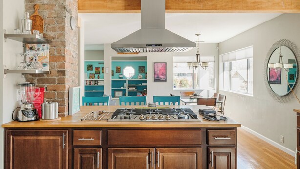 Una cocina con una isla central, pared de ladrillo, vigas de madera y una campana extractora moderna de acero inoxidable.