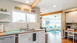 Cocina moderna con armarios blancos, encimera de madera y ventana. Hay letreros decorativos en la pared y se ve una parte del salón.