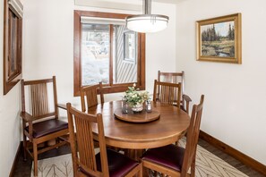 A wooden dining table with six chairs, a vase with flowers, and a painting on the wall.