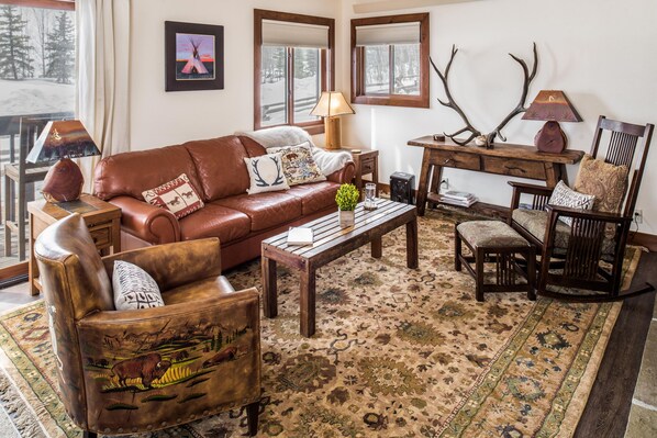 A cozy living room with a brown leather sofa, a wooden coffee table, and a patterned rug.