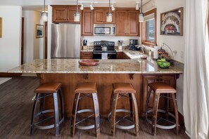 A kitchen with wooden cabinets, stainless steel appliances, a granite countertop, and four stools.