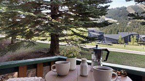 Una terraza de madera con una mesa dispuesta para café, una planta en maceta y una cafetera.