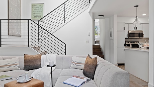 Una sala de estar moderna con un sofá gris, una mesa de centro y una escalera con barandilla negra.