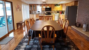 Comedor con una mesa larga, sillas de madera, cocina con armarios de madera, microondas y refrigerador.