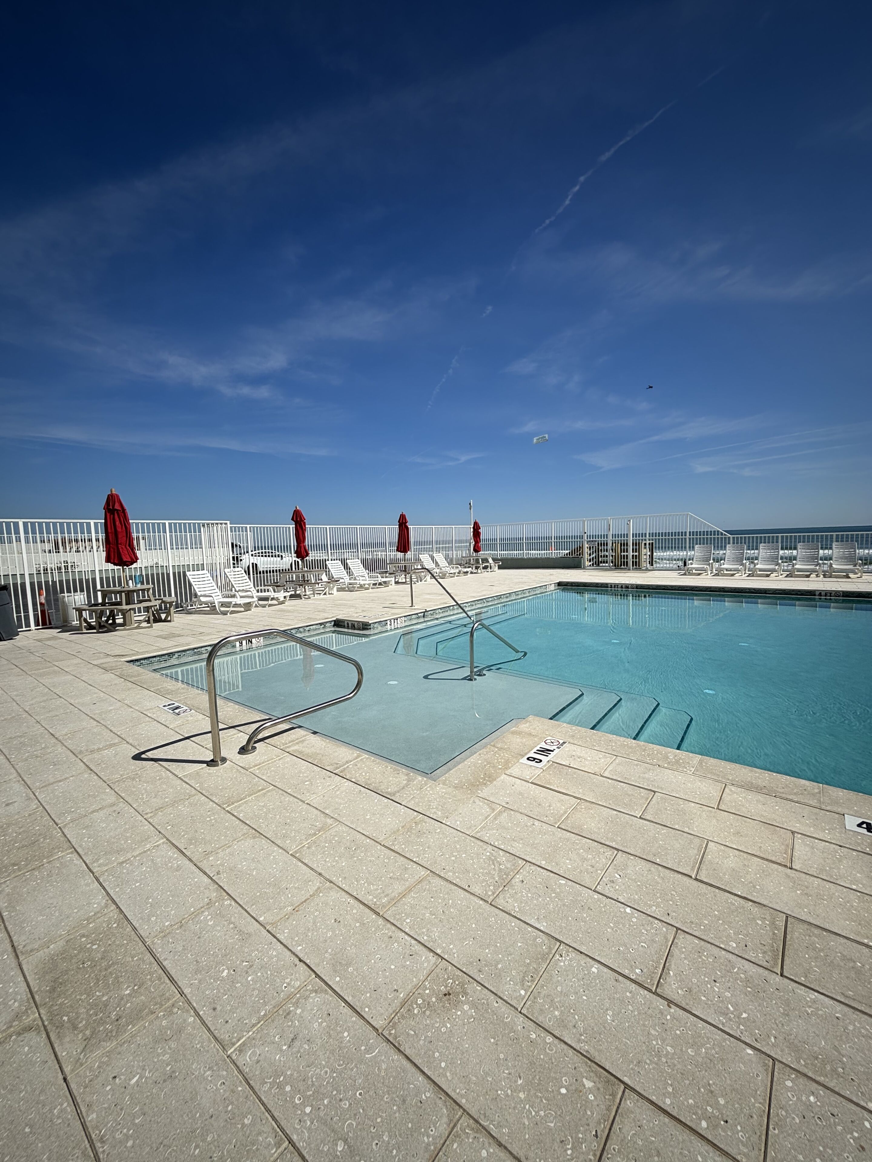Piscina com vista clara para o oceano, rodeada por espreguiçadeiras e guarda-sóis.
