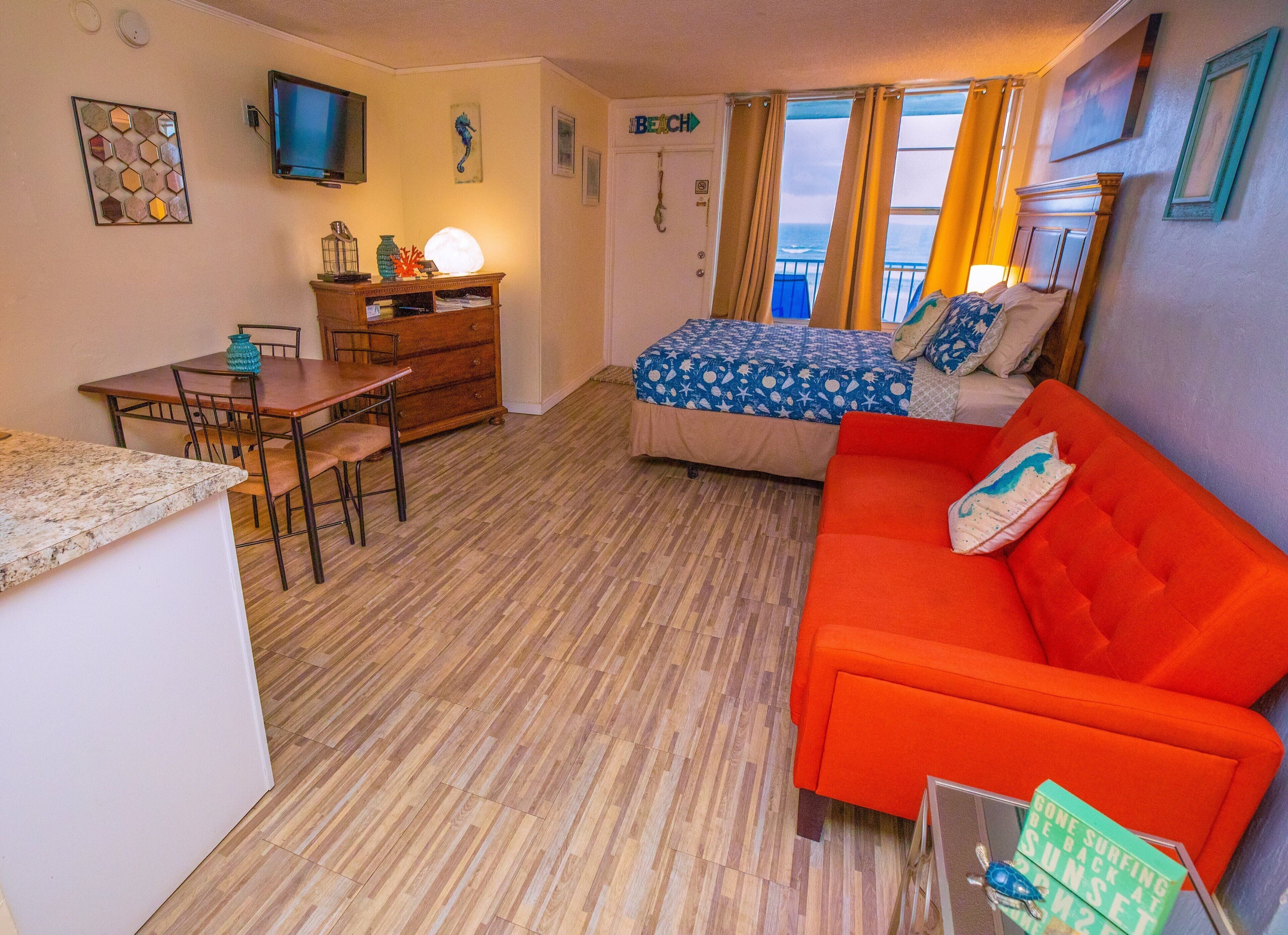 A compact room with a bed, a red sofa, a dining table, and a TV.