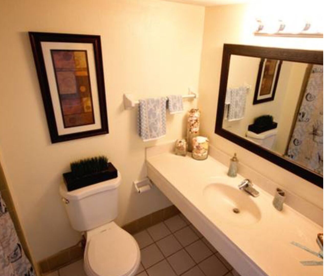 A bathroom with a toilet, sink, and mirror. There are towels and toiletries on the sink.