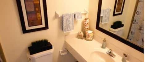 A bathroom with a toilet, sink, and mirror. There are towels and toiletries on the sink.