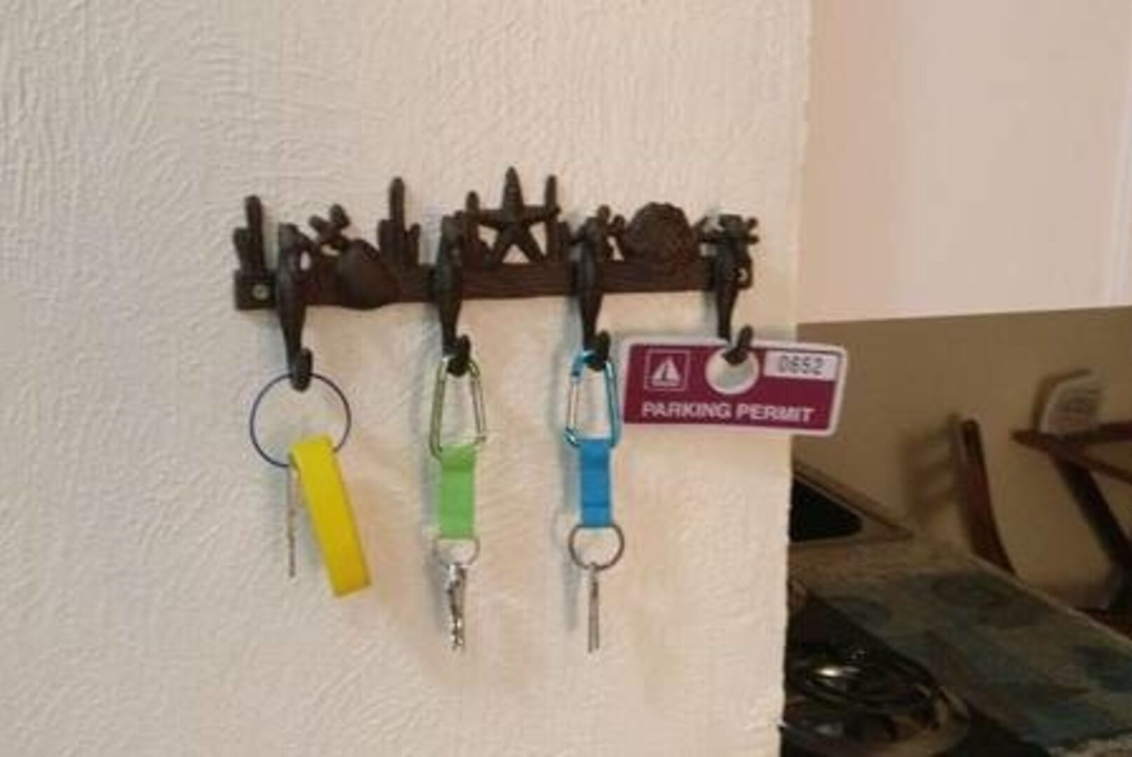 A wall-mounted key rack with three keys and a parking permit sign.