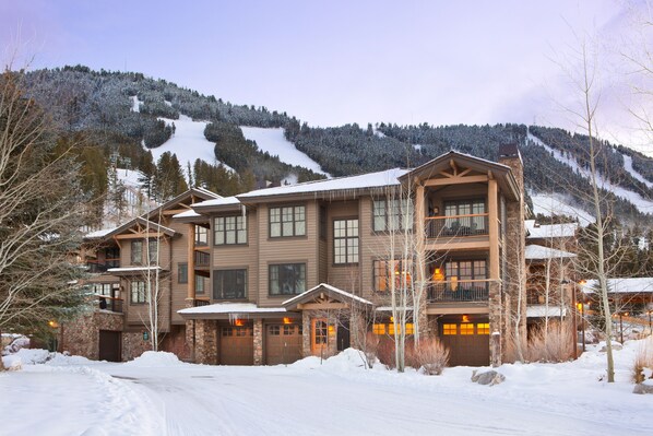 A multi-story lodge with a stone facade, multiple balconies, and a ski slope in the background.