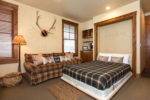 A bedroom with a plaid bedspread, a plaid sofa, and a deer antler wall decoration.