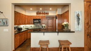 A kitchen with wooden cabinets, a central island with stools, a microwave, and a hanging light fixture. - Perfect location makes for easy access to downtown, Snow King and more (Jackson)