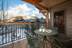 A wooden deck with a metal table and chairs, overlooking a snowy mountain.