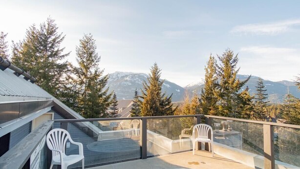 Una terraza en la azotea con un jacuzzi, dos sillas de plástico blanco y vistas a montañas nevadas.