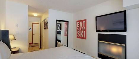 A hotel room with a bed, a TV mounted on the wall, and a sign that says "EAT SLEEP SKI".