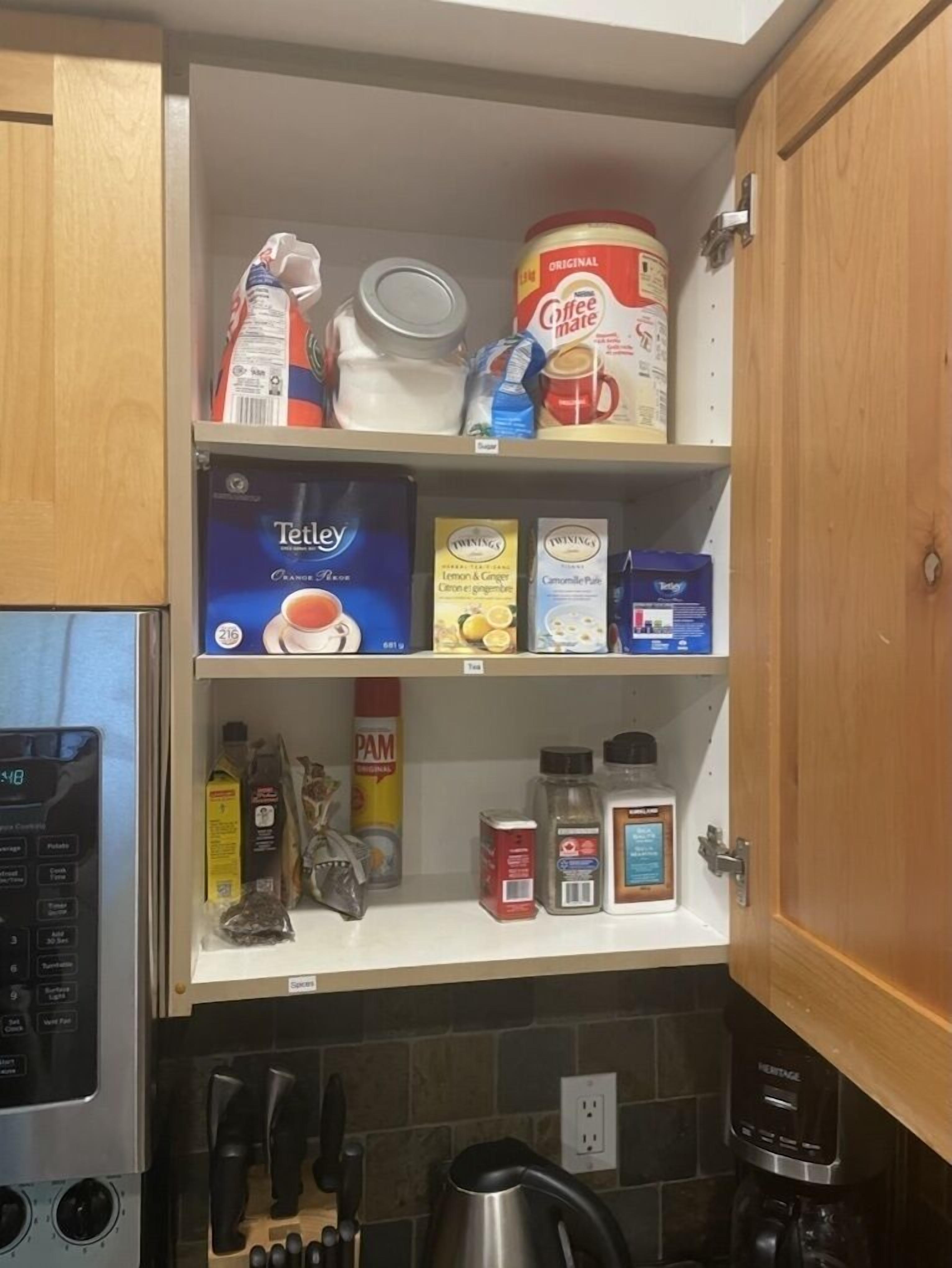 A kitchen with a coffee maker, a kettle, and various food items on shelves.