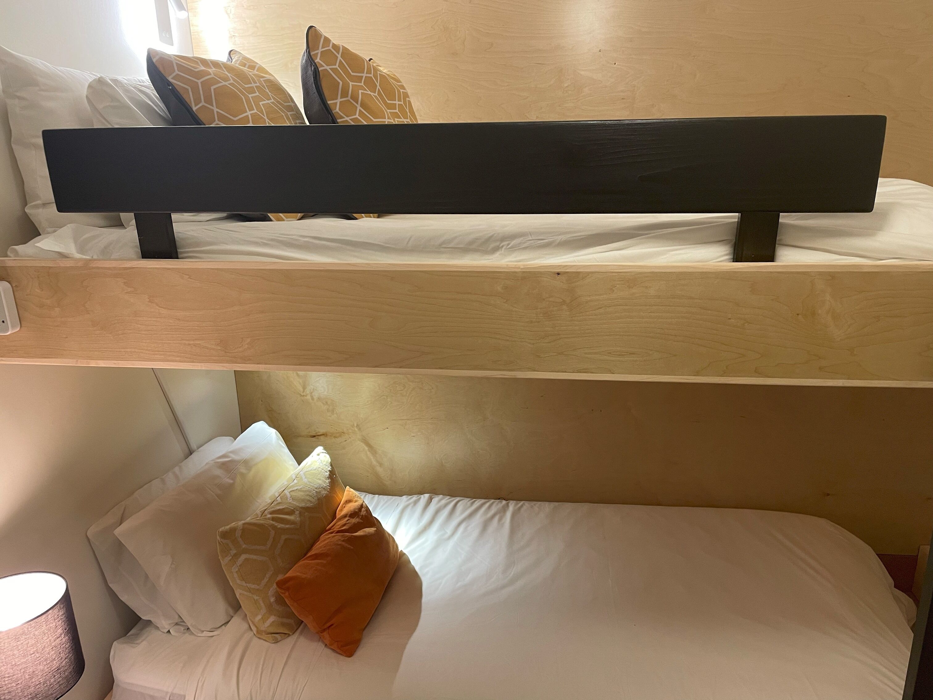Ein Etagenbett mit zwei Schlafstellen, jeweils mit weißer Bettwäsche und gemusterten Kissen.