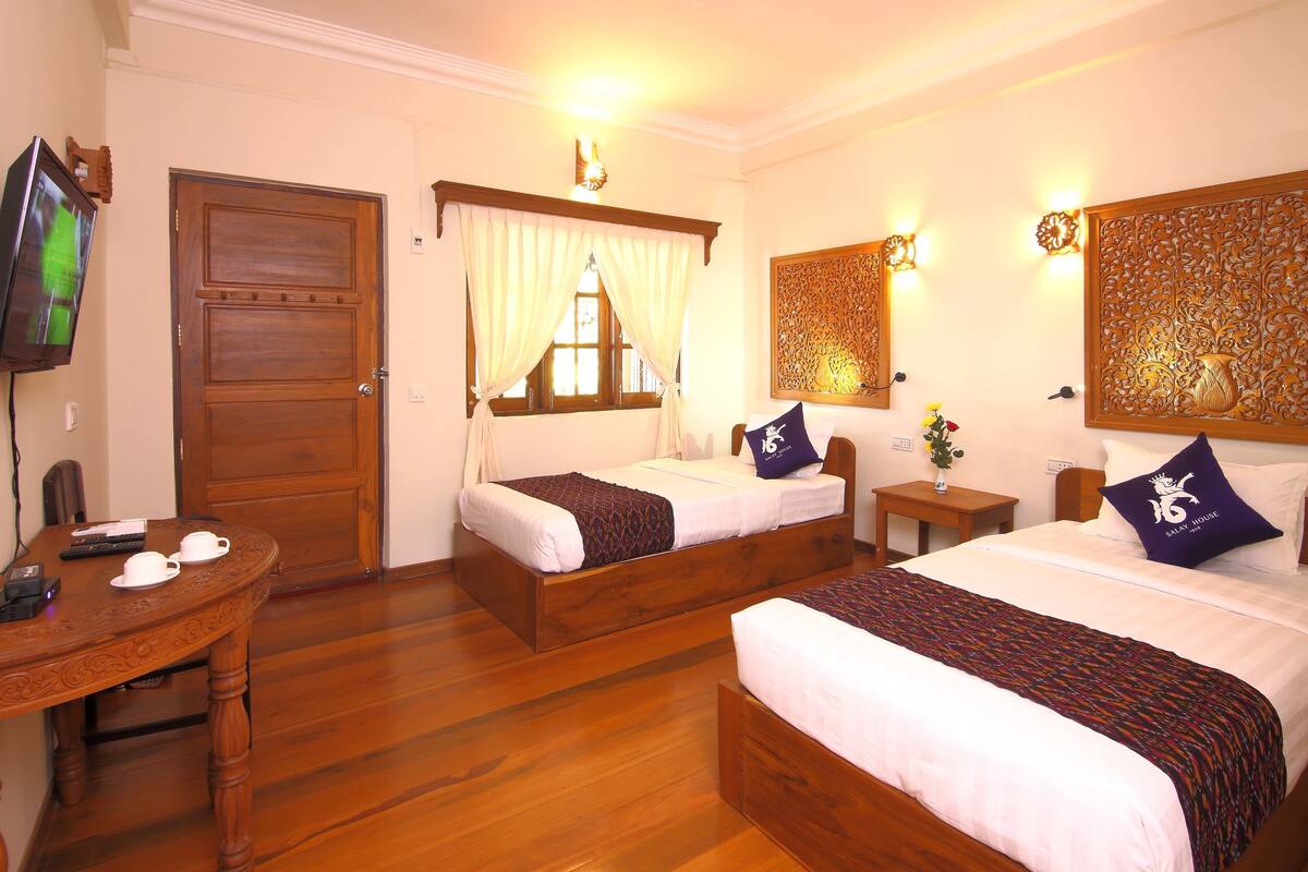A hotel room with two wooden beds, a wooden desk with a chair, a television, and decorative wall panels.