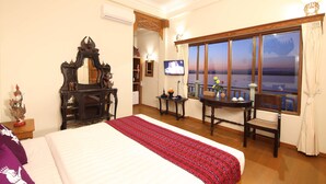 Quarto de hotel com cama, secretária com televisão, janela com vista e espelho decorativo.