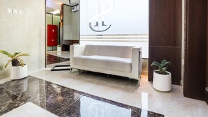 A modern lobby with a white sofa, marble flooring, and potted plants. - Sh Hotel (Ras Al Khaimah)