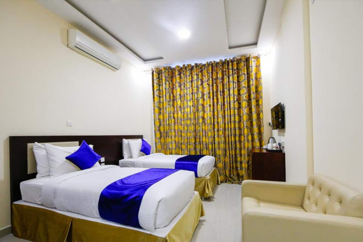Una habitación de hotel con dos camas, un sofá, un equipo de aire acondicionado y una cortina con un estampado amarillo.