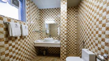 Et badeværelse med vægge af skakternet fliser, en vask, et toilet og et spejl.