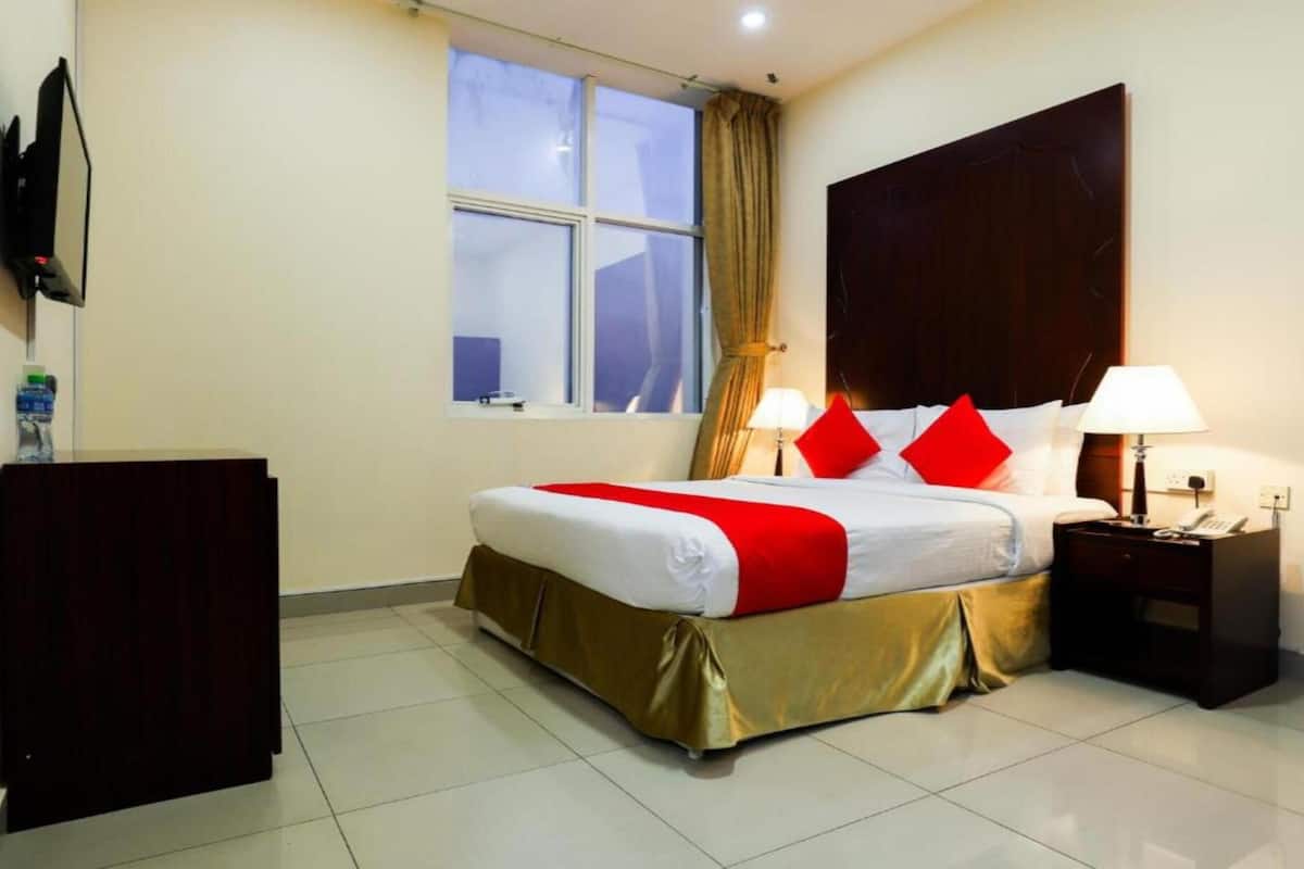 Habitación de hotel con cama, escritorio, televisión y ventana con cortinas.