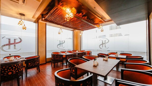 A restaurant interior with tables and chairs, a wooden ceiling, and hanging lights. - Sh Hotel (Ras Al Khaimah)