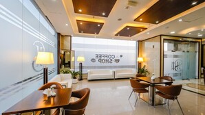 A modern coffee shop interior with seating arrangements, a coffee shop sign, and a glass wall. - Sh Hotel (Ras Al Khaimah)